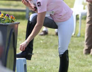 Stella Hagelstam taking off her spurs while reporting on her ride on the phone