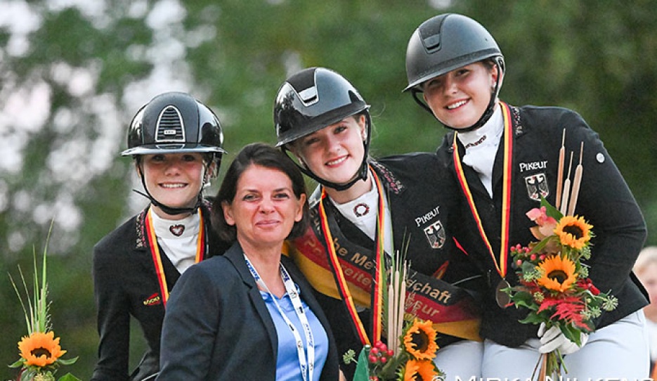 The pony podium at the 2026 German Youth Riders Championships with Kasselmann, Gosmann, and von Helldorff. Team trainer Caro Roost in front :: Photo © Mirka Nilkens