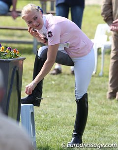 Stella Hagelstam taking off her spurs while reporting on her ride on the phone