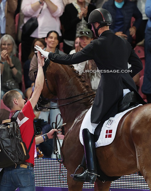 Groom Lars Seefeld high fives Daniel Bachmann Andersen who leaves the arena after his Kur to music ride on Marshall Bell at the 2022 World Championships Dressage :: Photo © Astrid Appels
